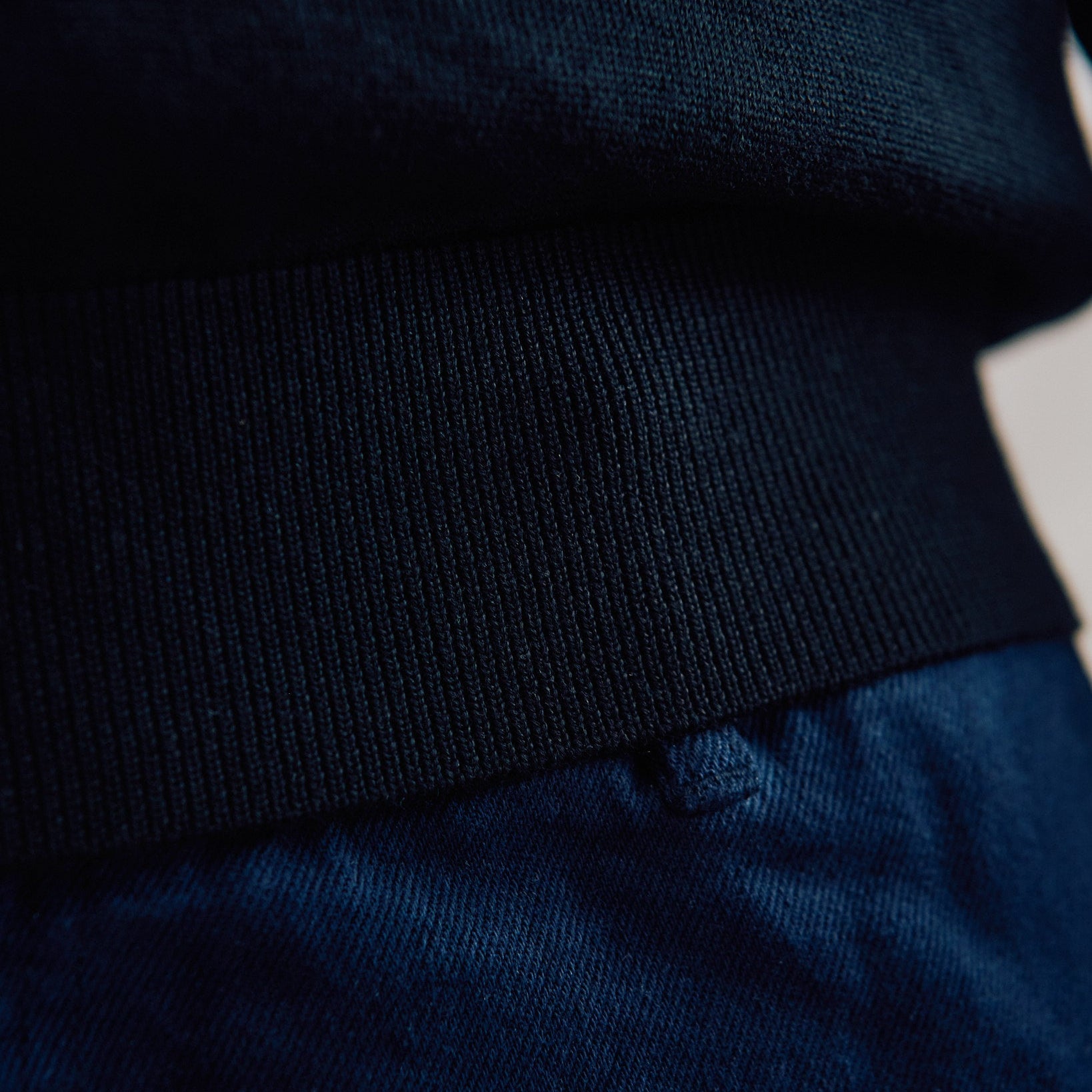 Close-up detail of a dark navy knit top with a wide ribbed waistband and matching navy fabric below.