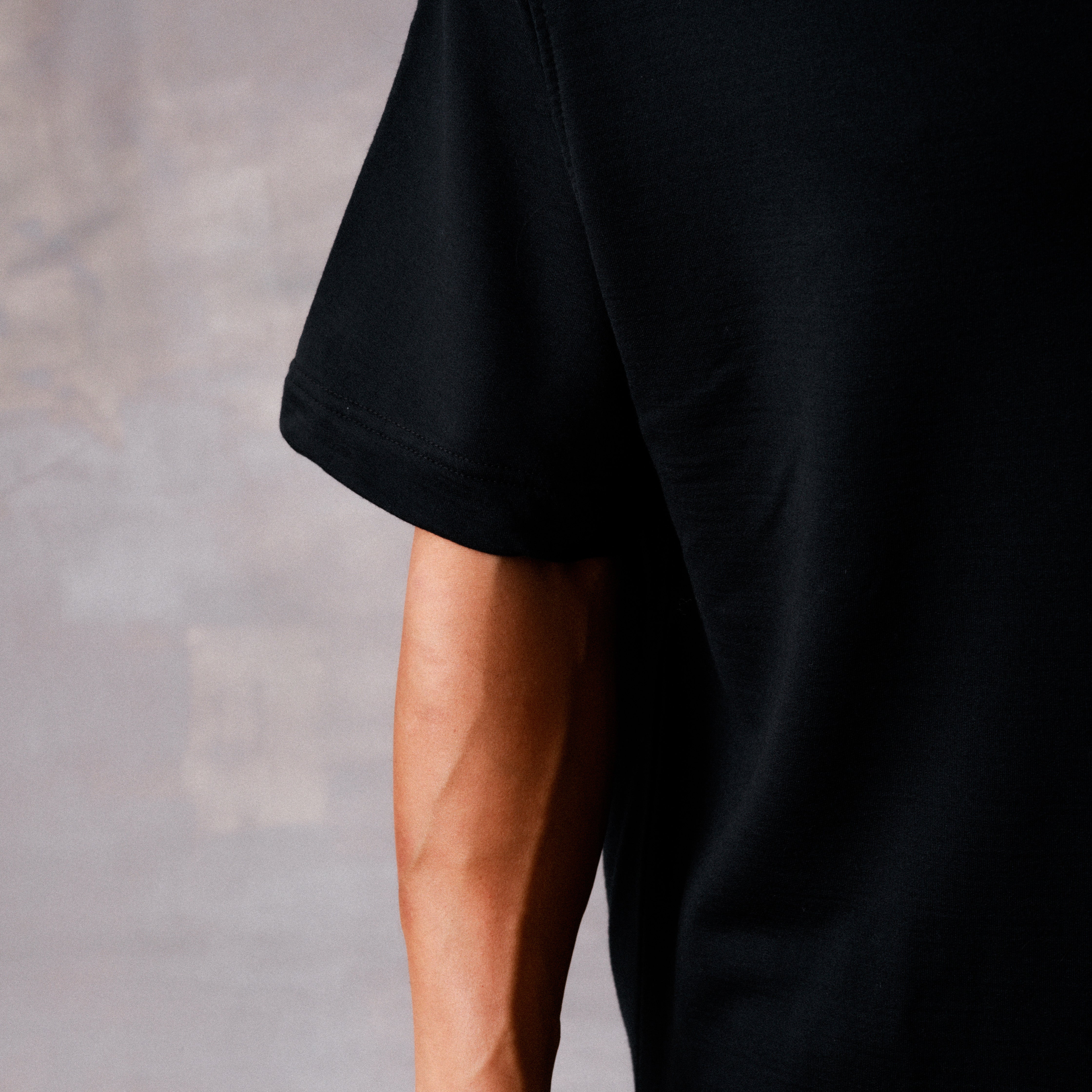 Black t-shirt draped over a person's arm on a neutral background