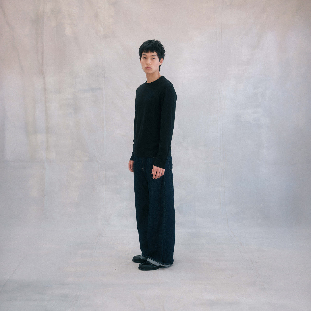 The Regular T-Shirt L/S in black extrafine merino wool, model wearing side view [model: tommy | size: S | length: Short]